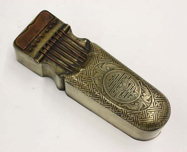 Chinese Brass and Copper Ink Writing Set: Chinese brass ink writing set with copper accents, the hinged lid cast as a qin partially hidden by a brocade patterned bag decorated with five bats encircling a shou medallion on a wanzi ground, the 