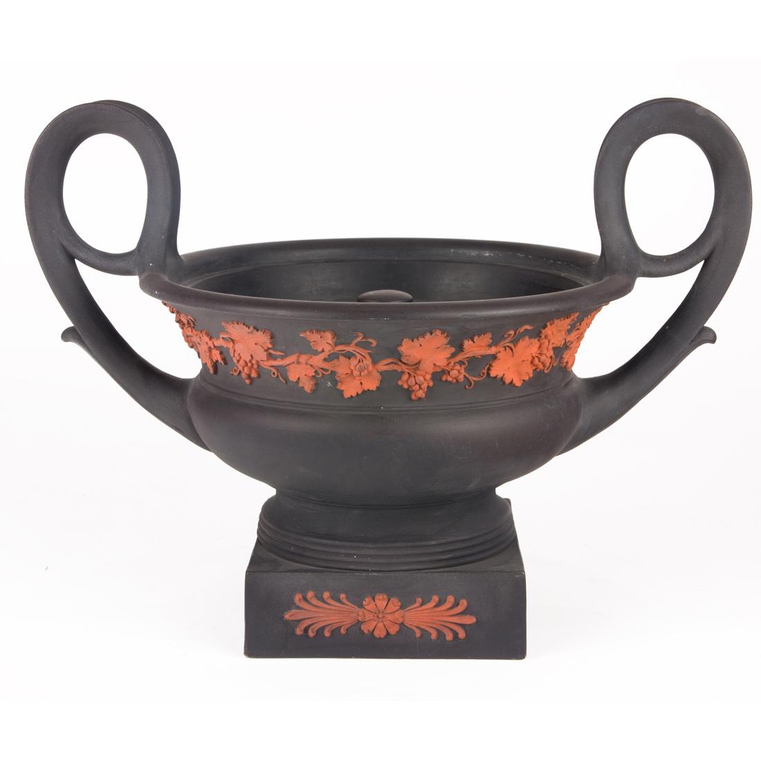 A Wedgwood black jasper crater form urn and cover: A Wedgwood black jasper crater form urn and cover, second quarter 19th century, applied with rosso antico fruiting grapevine band, florets and foliage, impressed 'WEDGWOOD' and 'RK', 8.25"h x 11"w (ac