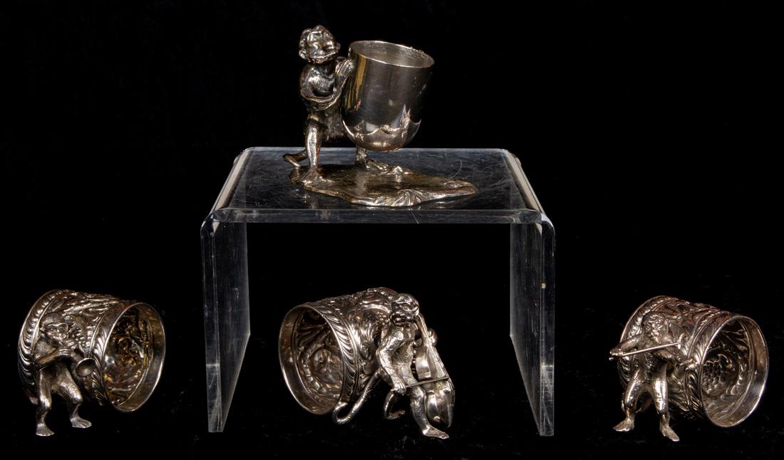 (Lot of 4) Aesthetic Movement three piece monkey band: (Lot of 4) Aesthetic Movement quadruple plate monkey singerie figural napkin rings, including a three piece monkey band with a cello, a trumpet and a violin player; the fourth, a monkey holding an ovi
