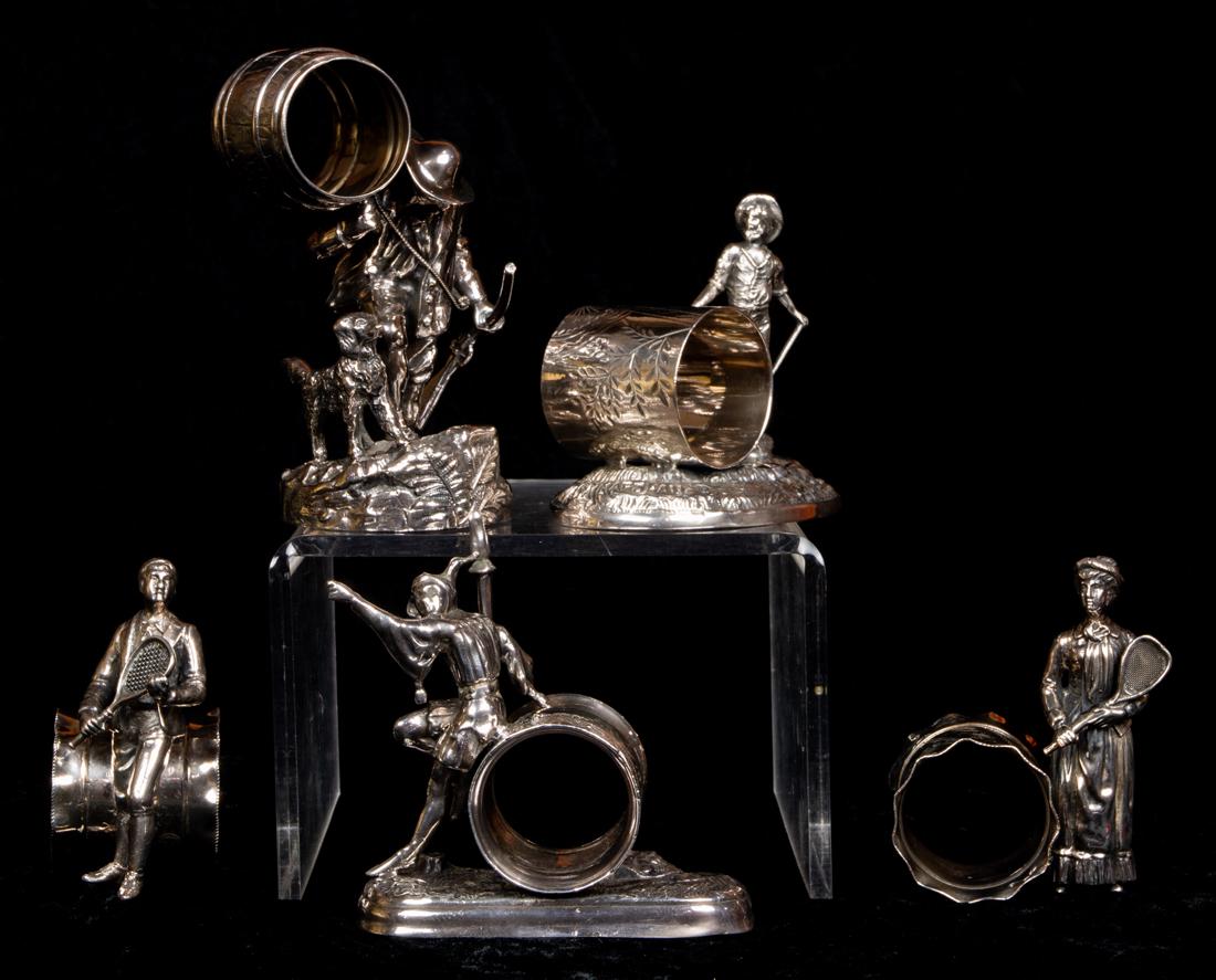 (Lot of 5) Aesthetic Movement figural napkin rings:: (Lot of 5) Aesthetic Movement quadruple plate figural napkin rings including a pair of male and female tennis players flanking a cylindrical form napkin ring; a Meriden & Co figure of jester leaning a