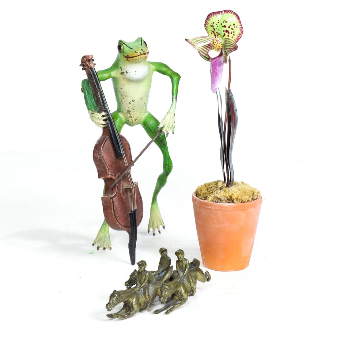 (lot of 3) metal decorations, including cold painted: (lot of 3) Metal decorations, consisting of cold painted figure of frog playing a cello, 7.75"h; a porcelain orchid in terracotta pot, 8.75"h and a figural group of three jockeys and horses, 4.75"l. P