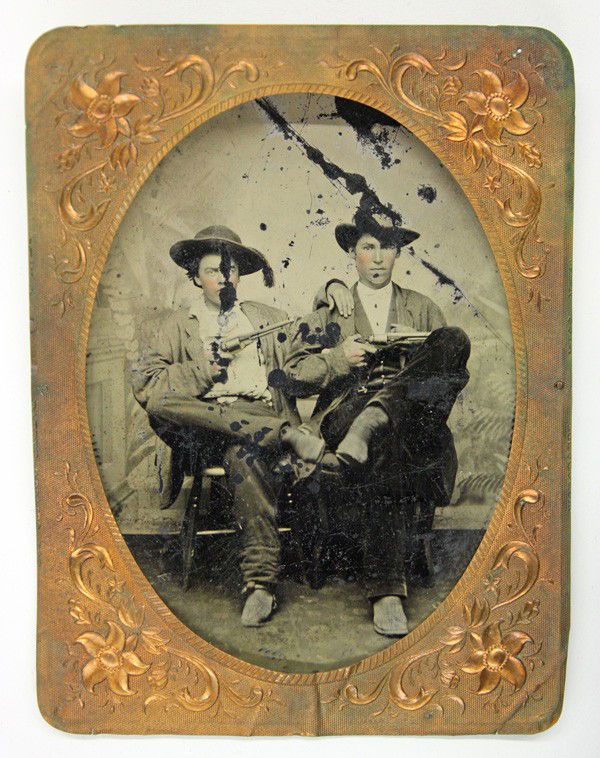 Tintype photograph of two cowboys: Tintype photograph of two cowboys, the cowboys are posed sitting down, displaying their Smith and Wesson revolvers, the image is housed with a copper matt with floral sprays, 4.25''h x 3.25''w