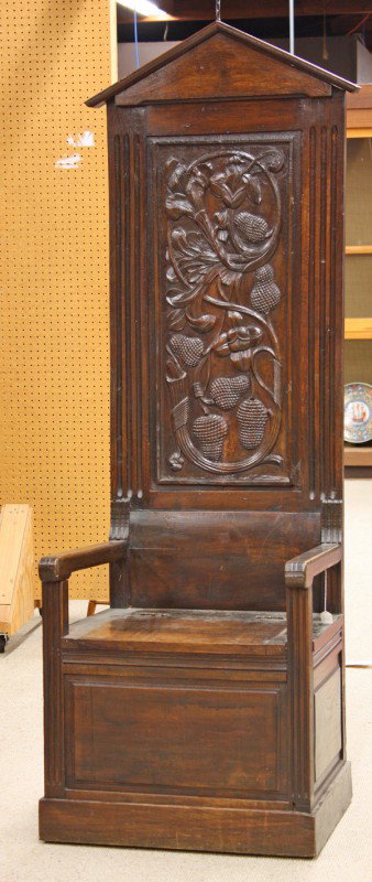 Renaissance revival bishops chair: Renaissance revival bishops chair, with a cornice above a carved panel with floral elements, above a hinged seat, with a conforming base, and plinth, 79''h x 26''w x 20''d