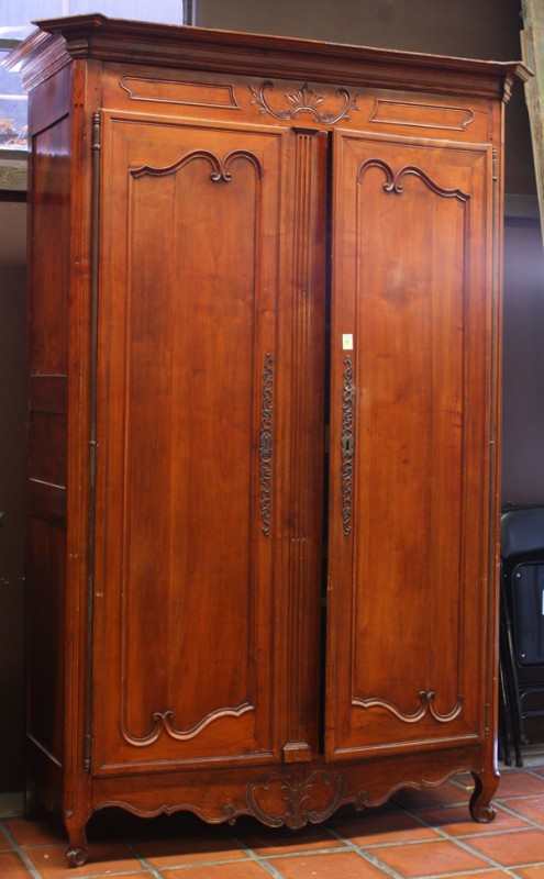 French Chateau Armoire: French chateau armoire circa 1800, executed in cherry and having a relief carved crest above the panelled doors retaining the original hinges and oversize escutcheons, rising on cabriole legs centered