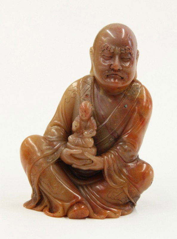 Chinese Soapstone Figural Carving: Chinese soapstone Buddhist figure, depicting a seated luohan (arhat) holding a Buddhist figure to the front in both hands, the stone possibly 'furong shi' and of a mottled pink hue with inclusions, 3.