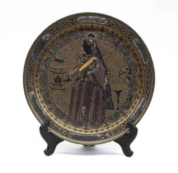 East Indian Inlaid Metal Plaque, Queen Victoria: East Indian gilt copper-alloy metal plaque with inlay of silver (oxidized) and copper, Colonial period, the circular tray-like plaque centered by a portrait of Queen Victoria holding a fan and standin