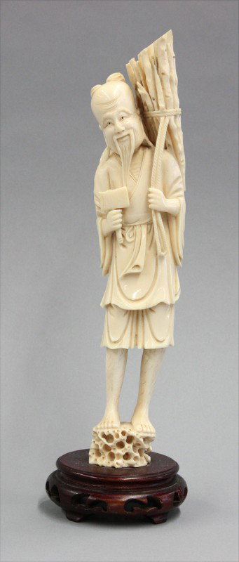 Chinese Ivory Figural Carving: Chinese ivory figural study of a woodcutter, Republic period, wearing a short tunic and a straw hat over his shoulder while standing on rockwork, a small axe held in his right hand, the other grasping