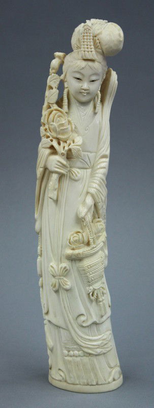 Chinese Large Ivory Figure of a Beauty: Chinese large ivory figural carving, depicting a celestial maiden standing in long robes and with a flower basket in her left hand, the other holding a floral spray partially framing her smiling face