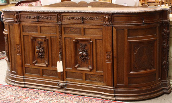 French carved oak sideboard: Monumental French oak buffet circa 1880, the rounded top above a conforming case with relief carved panels executed in the naturalistic taste and rising on a graduated molded base, 42''h x 97''w x 25'
