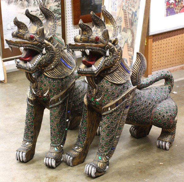 Asian Inlaid Wooden Lions: Pair of Southeast Asian gilt and mirror-glass inlaid wooden mythical leonine zoomorphs, each with large red bulging eyes and large gaping month with a large red tongue, the head topped by three shaped