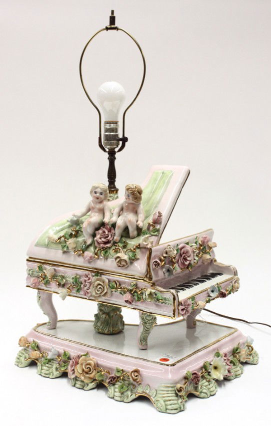 Italian figural lamp: Italian figural lamp executed in the Capodimonte style, the single light supported by a concert grand piano surmounted with putti and embellished with applied floral sprays and rising on a conforming