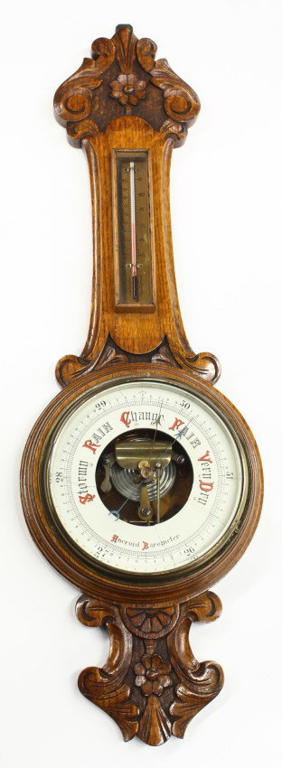 English oak barometer: English oak Aneroid banjo barometer circa 1890, having a carved case with rosette medallions flanking the circular bevelled glass measuring window, 33''h x 10''w