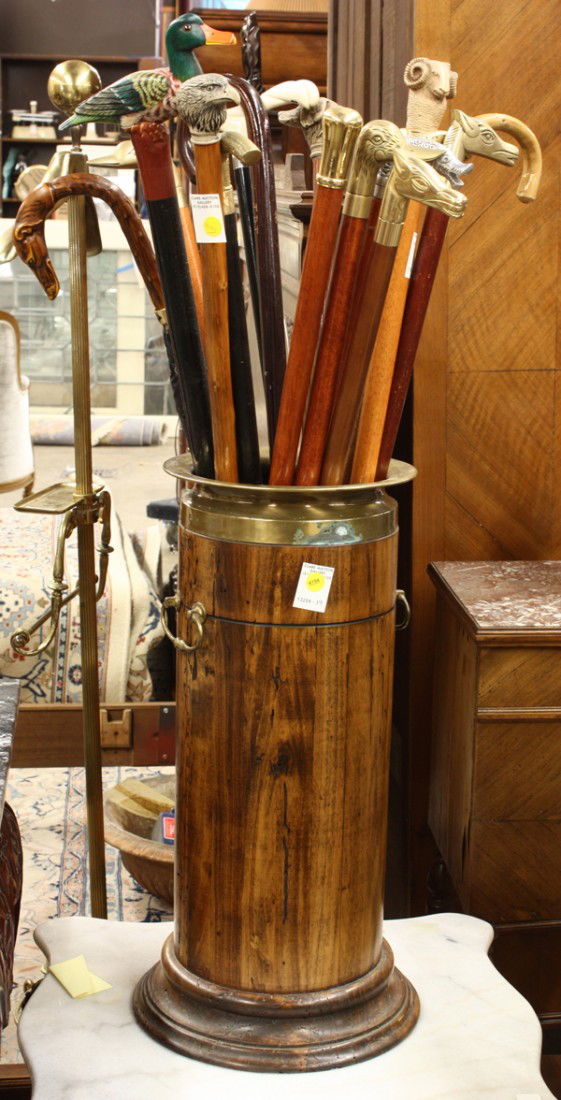 Walking stick group: (Lot of 17) Collection of walking sticks, including brass figural head sticks depicting a Greyhound, ram, ducks, etc contained in a columnar cane holder having a outswept brass rim and terminating on