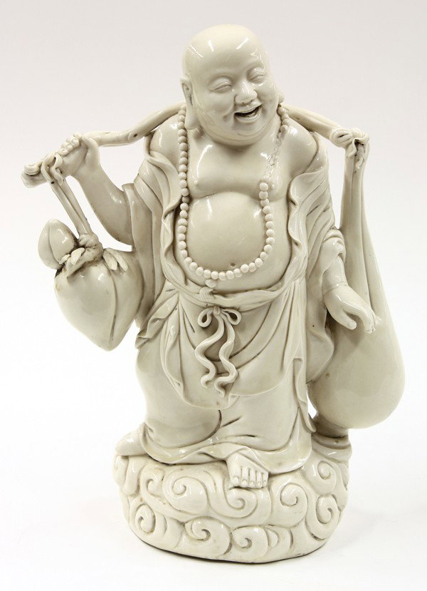 Chinese Blanc de Chine Figure of Budai: Chinese Dehua (blanc de Chine) figure of Budai, the Buddhist deity with a joyous smile and full belly, the standing figure wearing monastic robes and featured with large treasure sacks suspended at ea