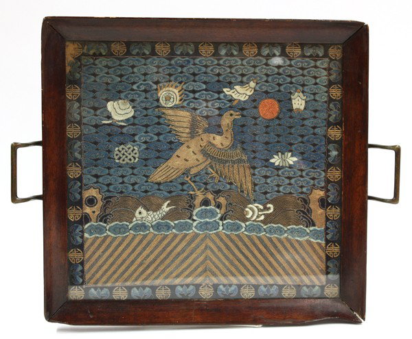 Chinese Rank Badge Set Into a Tray: Chinese rank square mounted in a tray, late Qing dynasty, the rank square couched with a golden bird set against a cloud embroidered ground scattered with the eight Buddhist emblems, above cresting wa
