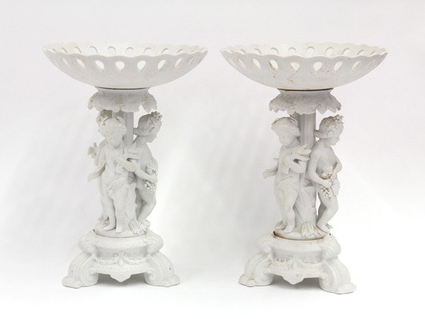 Neoclassical style compotes: Pair of parian ware figural compotes, in the Neo-Classical style, having a reticulated bowl supported by a fluted column surrounded by three cherubs, 12''h