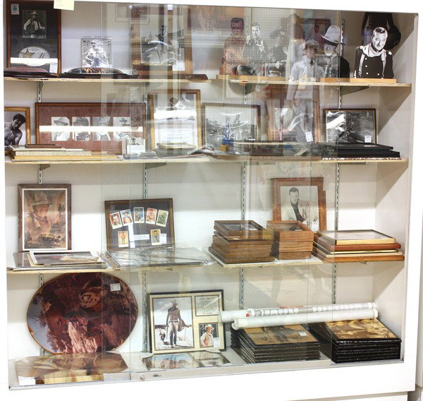 John Wayne ephemera: (lot of one case) Framed John Wayne ephemera including photo reproductions, signed portraits, cut out images, etc