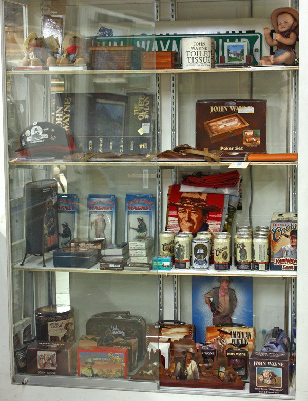John Wayne memorabilia: (4 shelves) John Wayne associated memorabilia, including street signs, toilet paper ''Its Rough it's Tough and it Doesn't Take Cr.. Off Anyone'', bears, pencils, caps, poker set, playing cards, Coors 