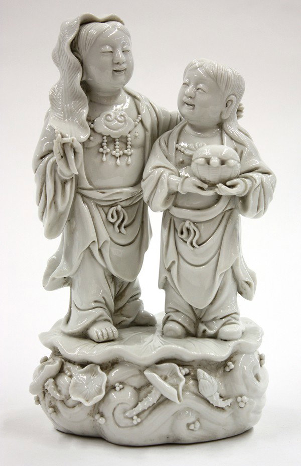 Chinese Blanc de Chine Dehua Figure, Hehe Erxian: Chinese Dehua porcelain figural group, featuring the Buddhist acolytes Hehe Erxian with one wearing a ruyi form necklace and holding a large leaf gracing his head, standing next to his companion clutc