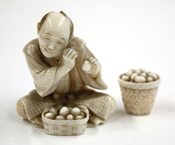 Japanese Ivory Carving, Man and Eggs: (Lot of 2) Japanese figural ivory carving (okimono), fashioned with a seated farmer with head tilted and eyes winked looking at an egg through a scope he created with his right hand, above a small bas