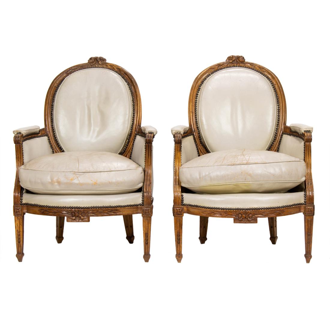 A pair of Louis XVI style bergeres 1890-1910: A pair of Louis XVI style bergeres 1890-1910, with an oval back having a carved crest, the leather upholstery with brass nail head trim, and rising on carved and tapered legs, 40"h x 28"w x 21"d