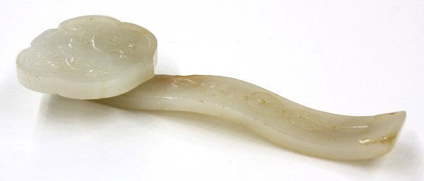 Chinese Jade Ruyi Scepter: Chinese jade/jadeite carving of a ruyi scepter, the ruyi head framing a pair of large pomegranates in sunken relief above the contoured shaft carved with a bat suspending two linked coins, the semi-tr
