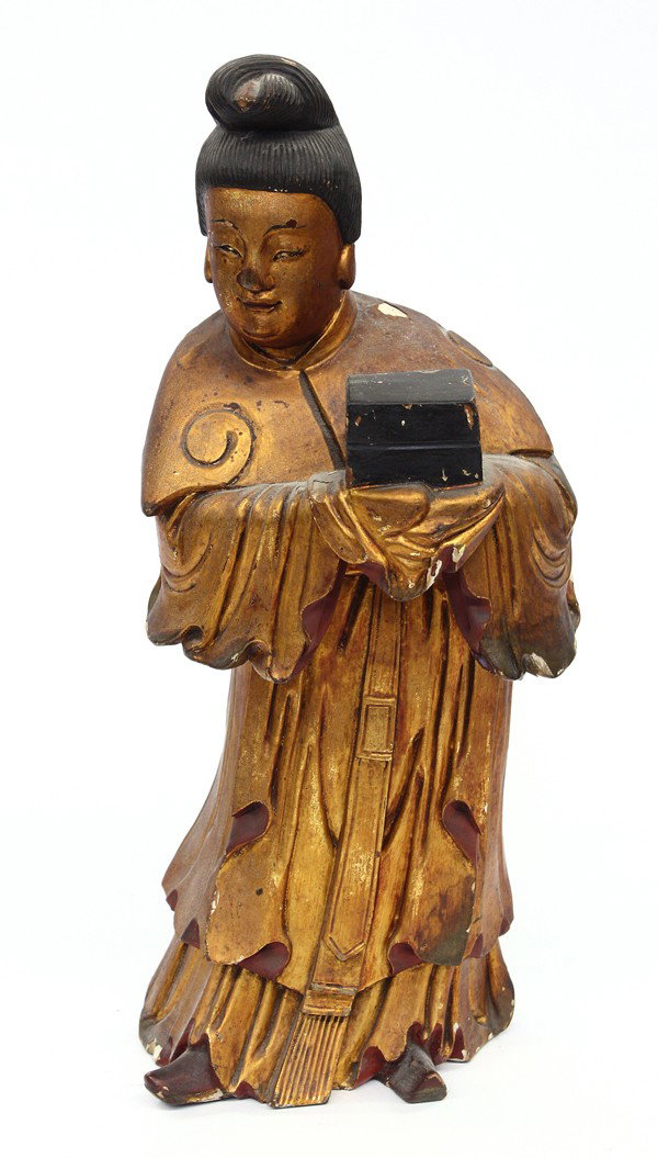 Chinese Gilt Lacquered Wood Figure: Chinese gilt and lacquered wooded figural carving, the standing maiden with a sincere face framed by a neatly piled chignon, her full figure draped in tiers of loose robes and holding a stack of two b