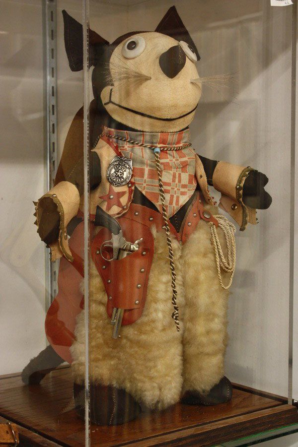 Western items: Circa 1940 Felix The Cat depicted as a Deputy Sheriff Cowboy wearing wooly chaps, with lasso, vest, bandana, and hat, standing on a custom oak base with an acrylic cover, 19'' without hat