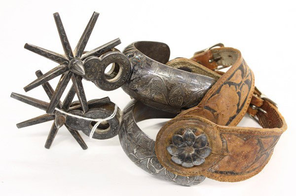Western spurs: (lot of 2) Pair of Charro spurs in the Vaquero tradition showing engraved silver decoration, having an eight point spoke rowel, flower formed concha, and tooled spur leather
