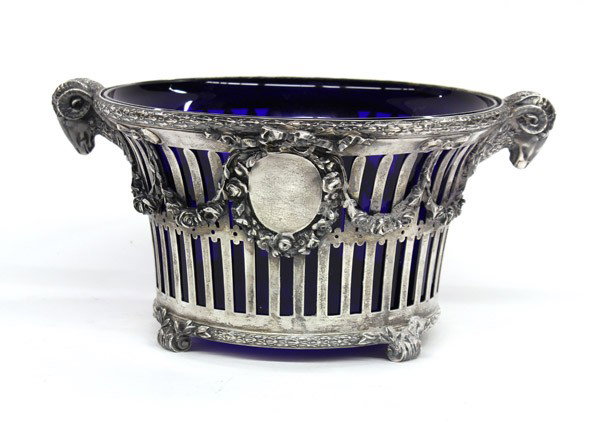German .800 centerpiece: German .800 reticulated centerpiece decorated with bows, floral swags and medallions flanked by ram head handles with a cobalt glass insert, 6''h 12''w, 41.13 troy oz.