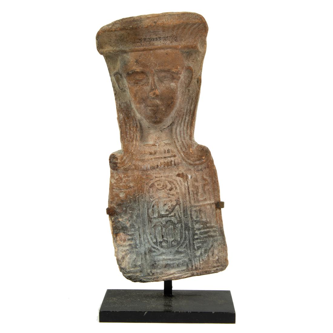 A Grand Tour Egyptian style red clay hieroglyphic panel: A Grand Tour Egyptian style red clay hieroglyphic panel headed by a head 6"h x 2.5"w, mounted on modern weight black metal stand. Provenance: Property from a prominent San Francisco estate