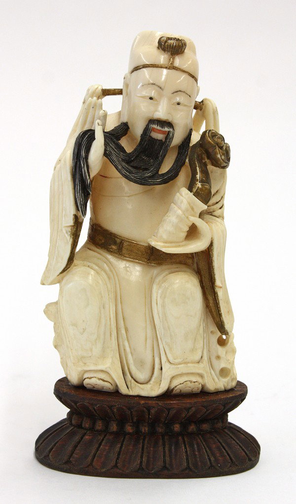 Chinese Ivory Figure of a Court Official: Chinese ivory figural carving, probably Lu of the Three Star Immortals stroking his long beard while holding a ruyi scepter and seated on a rocky plinth, with dark pigment and gilt accents, ivory: 5''
