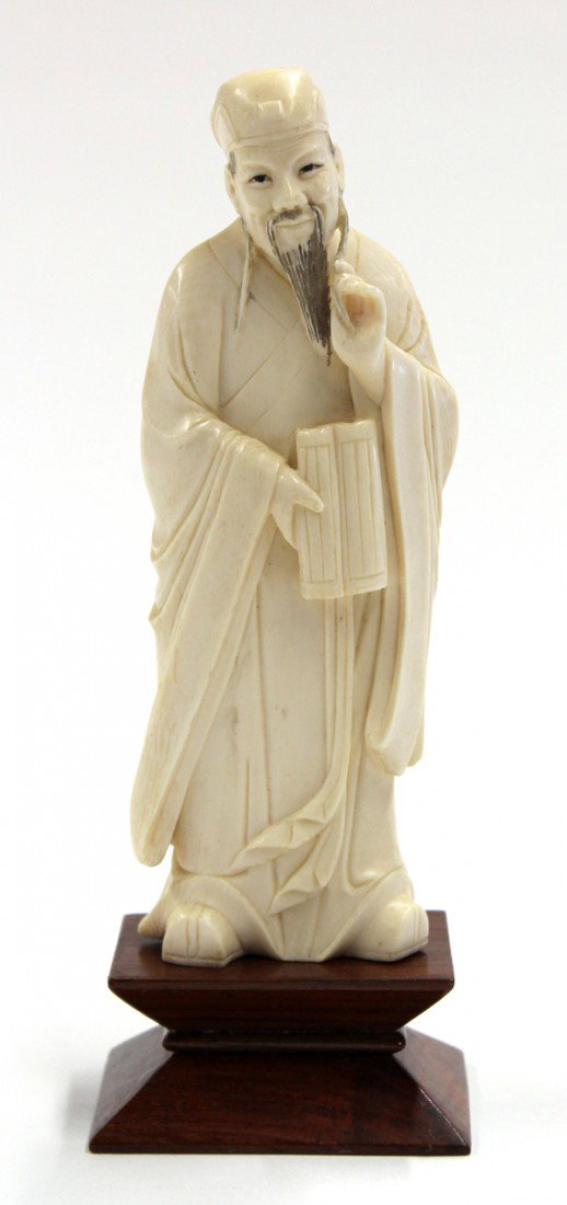 Chinese Ivory Carved of a Sage: Chinese ivory figural carving of a scholar, standing in long flowing robes with a partially open book held in his right hand, the left hand fingering his long dark-tinted beard, a close-fitting schola