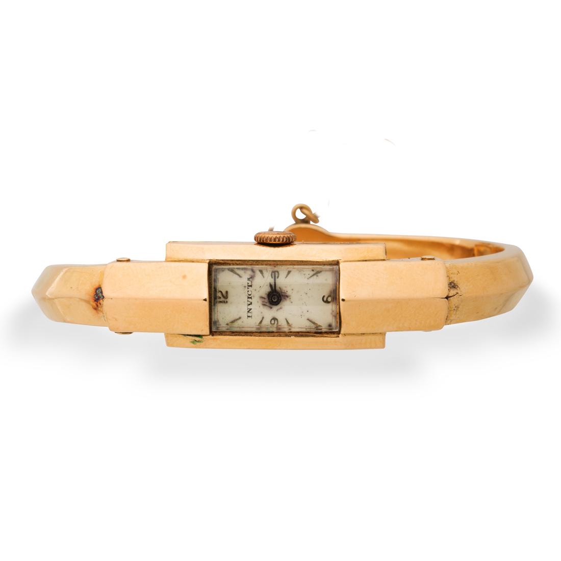 An eighteen karat gold watch bracelet, Invicta: An eighteen karat gold watch bracelet, Invictathe rectangular cream dial, with baton hours and hands, within polished gold case, containing a eighteen jewel manual movement, on polished hinged bangle
