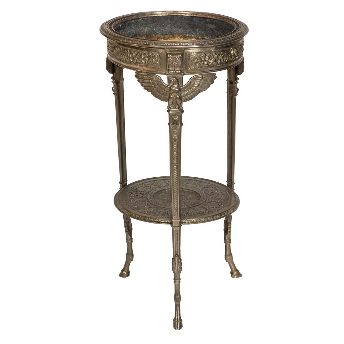 An Empire style silvered metal jardiniere: An Empire style silvered metal jardiniere, having a circular top with a lined interior, above eagle accented legs continuing to a lower tier, and rising on hoof feet, 29"h x 14"dia.