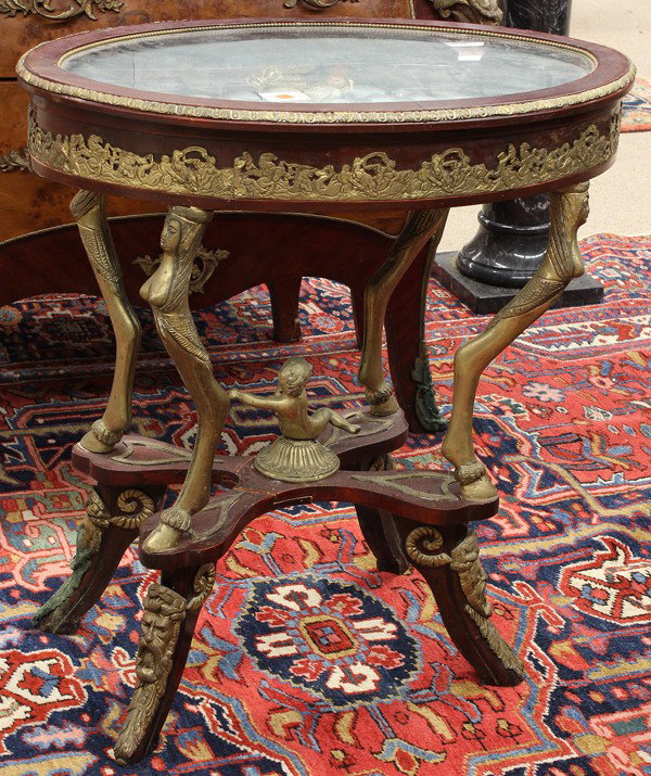 Empire style table vitrine: Empire style bronze mounted table vitrine, the oval hinged top opening to the lined and tufted interior, the exterior with applied mounts depicting a Classical scene, above bronze figural supports cen