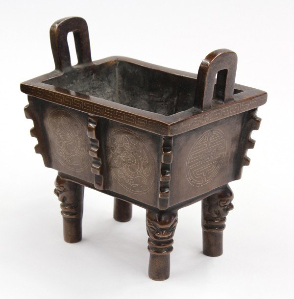 Chinese Silver Inlaid Bronze Censer: Chinese patinated bronze censer with silver inlay, of rectangular ding-form with notched flanges framing the silver inlaid dragon roundels and shou medallions below the key-fret heightened rim, furthe