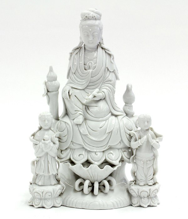 Chinese Blanc de Chine Buddhist Group: Chinese blanc de chine Buddhist figural group, centered with Guanyin seated on a lotus pedestal in lalitasana while holding a scroll in her hand, bracketed by the youthful attendants Jintong and Yunu,