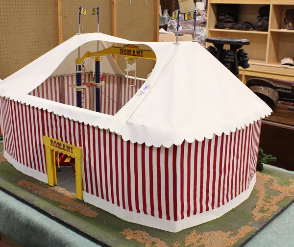 Model circus tent: Model circus tent, mounted on a simulated lawn, having white and red stripes, the roof opening to an interior with trapeeze, clowns, giraffes, and tigers, 24''h x 47.5''w x 32''d
