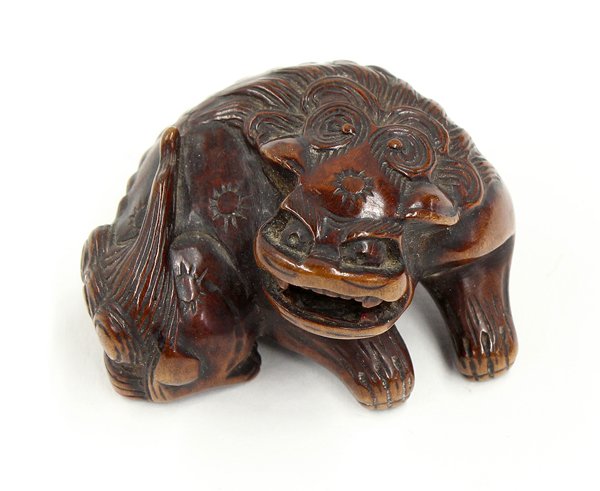 Japanese Boxwood Netsuke, 18th century: Japanese boxwood netsuke of a karashishi, Edo period, 18th century, the recumbent leonine figure with its body curled and head raised, the open mouth with a small free-moving ball, 1.75''l. Provenance