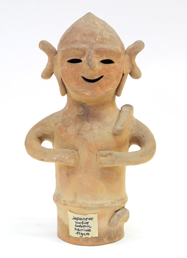 Japanese Haniwa Pottery Figure: Japanese haniwa pottery figure, fashioned as an entertainer with a broad smile, pointed headdress, large earrings below knotted tresses, its stylized arms held to the front, 15.25''h. Provenance: Prop