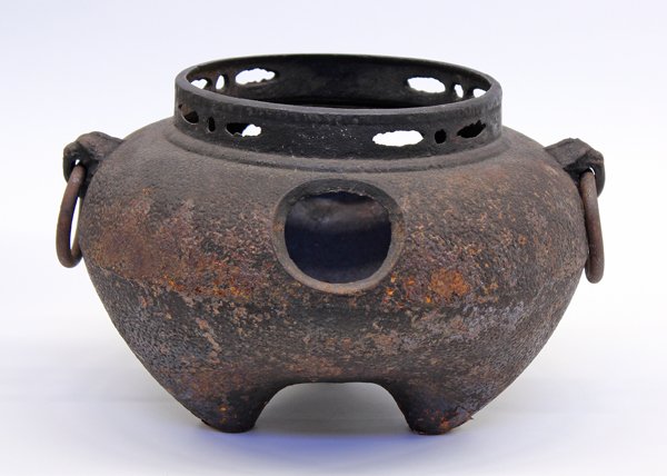 Japanese Cast Iron Tea Ceremony Brazier: Japanese iron tripod brazier, of compressed ovoid shape raised on three conical supports, cast with a textured surface with two apertures, a short pierced neck and pair of animal-mask and loose ring h