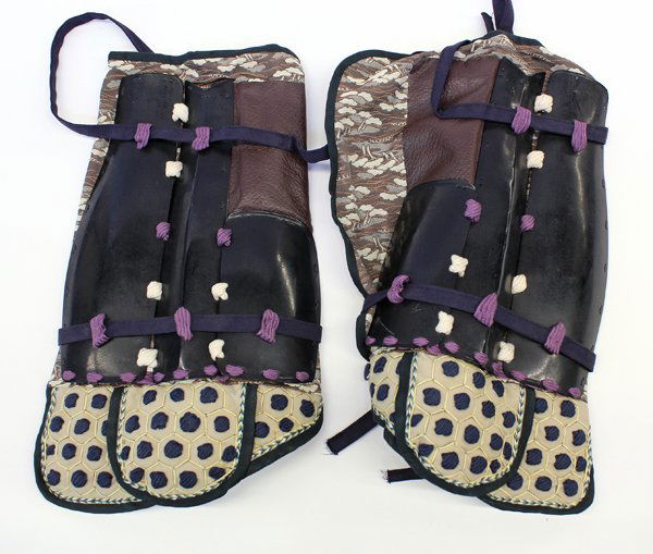 Japanese Armor: Shin-Guards: Japanese iron and cloth sune-ate (shin armor), each composed of three black lacquered metal plates attached to a brown leather and brocade-fabric backing, the upper section with dark blue cording in a