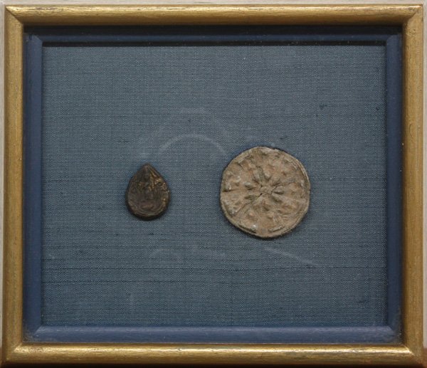 Thai Buddhist Amulets: Framed Thai Buddhist amulets, one of tear-drop shape and impressed with a Buddha, the other circular with an abstract design, together with a tag identifying the work as 'Pong Supan, from Supan Provin