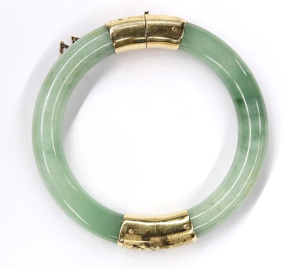 Jadeite hinged bangle with 14K fittings: One jade two toned hinged bangle bracelet with 14K (stamped) yellow gold clasp and fittings, mounted on clasp with (1) 0.10 ct. round cabochon cut green jadeite stone and measuring 8.75'' around and 8