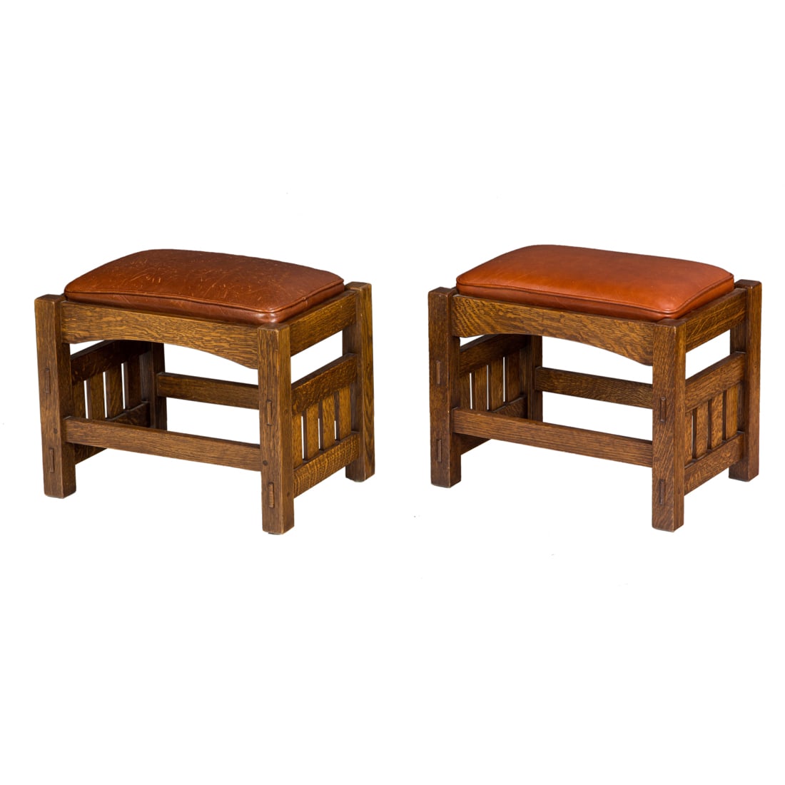 A pair of Voorhees Craftsman Arts and Crafts style footstools: A pair of Voorhees Craftsman Arts and Crafts style footstools, each with leather drop in seats above the base with an arched apron, slatted sides with pinned thru tenon construction and rising on squa