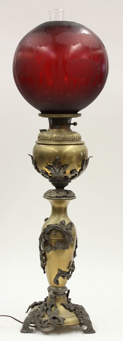 Victorian Gone With the Wind lamp: Victorian Gone With The Wind lamp, having a cranberry shade accented with lotus blossom reserves, above a brass ande patinated metal base rising on Rococo style feet, 38''h