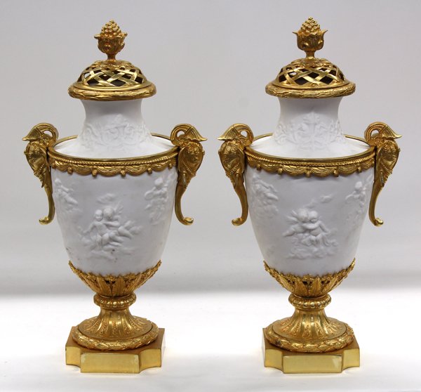 Louis XVI style ormolu mounted urns: Pair of Louis XVI style white porcelain ormolu mounted urns, having a reticulated and finial capped cover above the shouldered bisque form having winged putti reserves flanking the tapering body, set 