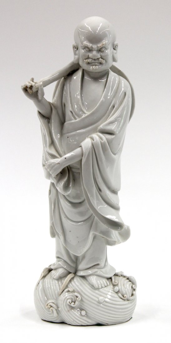 Chinese Blanc de Chine, Luohan: Chinese blanc de chine porcelain luohan, the Buddhist arhat standing on rolling waves and picked out with exaggerated features, with a hat hanging on the staff slung across his shoulder, while the lef