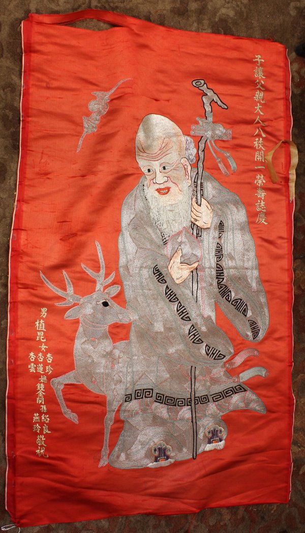Two Chinese Embroidered Hangings: (Lot of 2) Chinese metallic couched hanging of Shoulao, with benevolent face bearing a full beard embroidered with colored threads in satin stitch, contrasting with the body couched in metallic thread